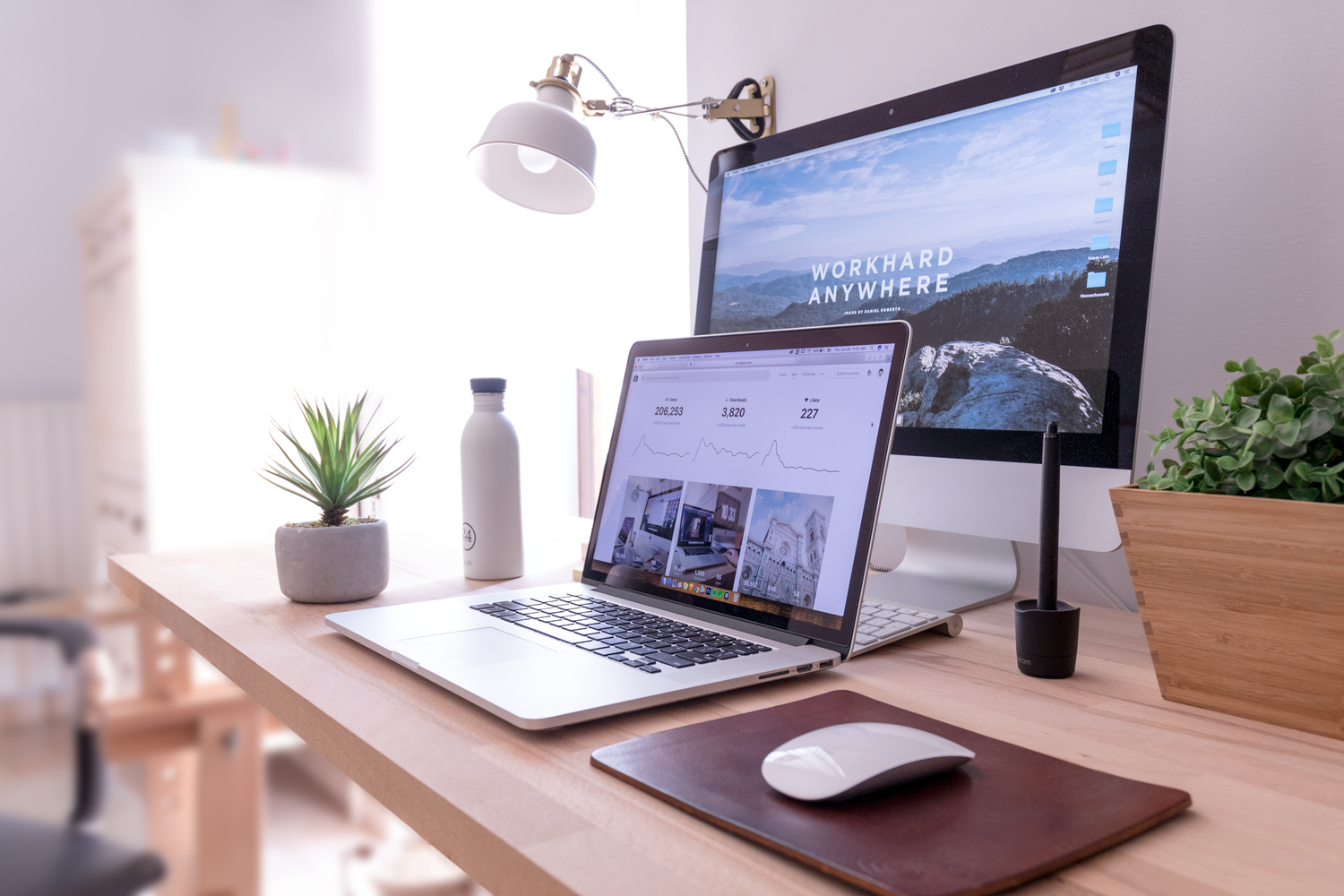 Desk with a laptop and monitor showing a travel website