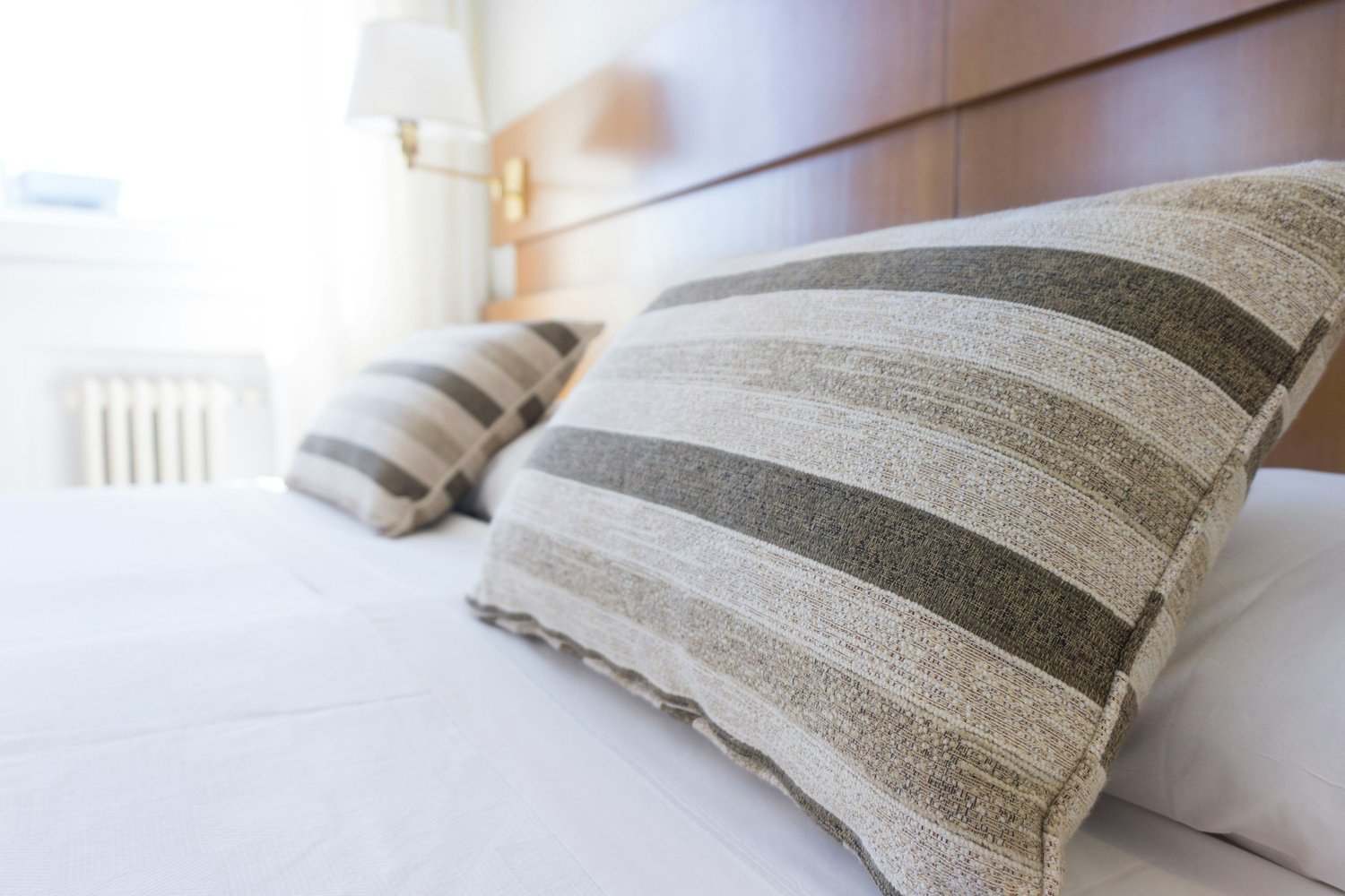 Close-up of striped linen pillows on a crisp white hotel bed in morning light