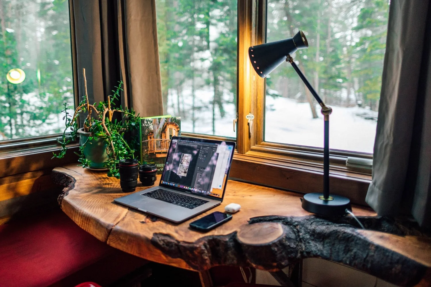 Laptop on a live-edge wooden desk by a window overlooking snowy pines