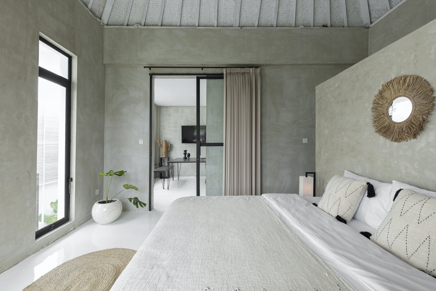 Minimalist concrete-and-linen bedroom with a rattan mirror and garden view