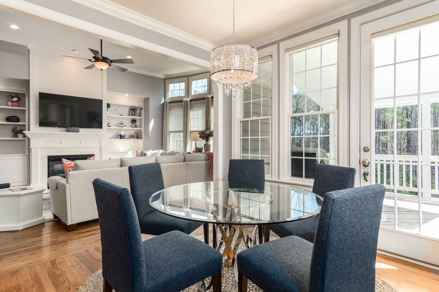 Dining area with a glass table, navy chairs and a crystal chandelier beside French doors